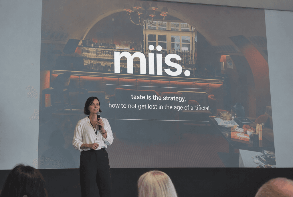 A speaker with a microphone in front of a projected miis. slide reading “taste is the strategy”