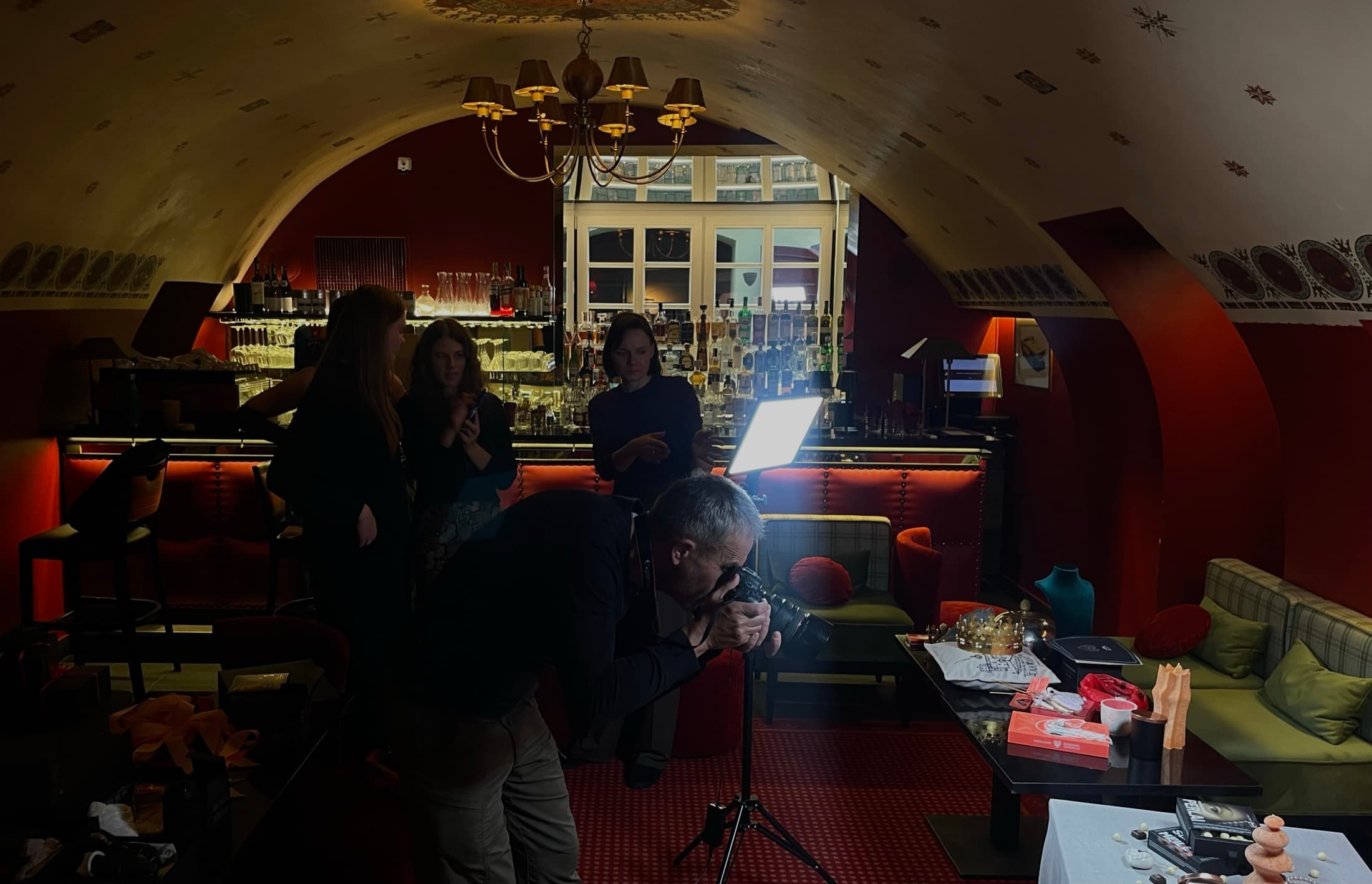 A vaulted room at night under red light, a bar along one wall and people at the tables