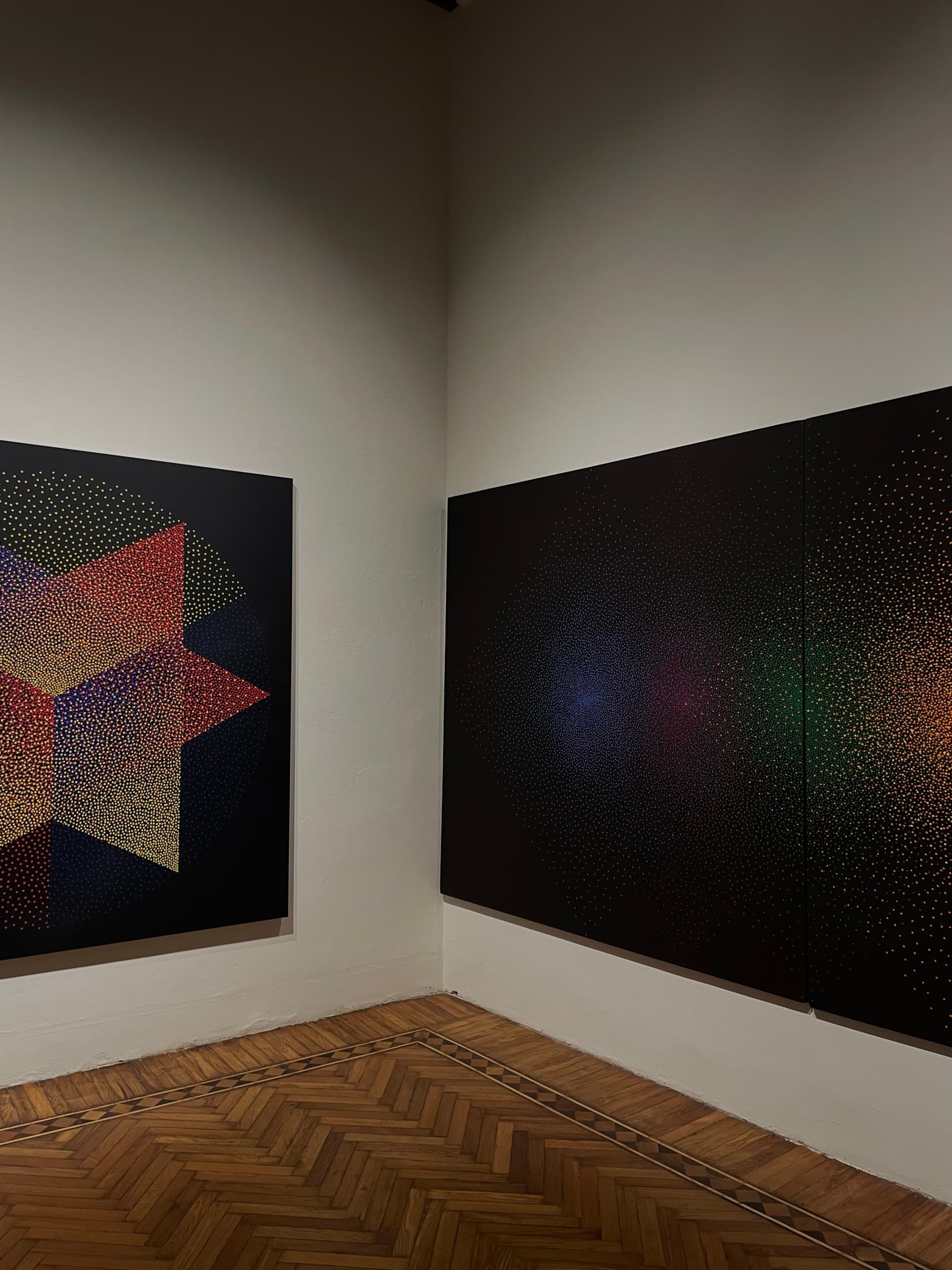Two large dot-pattern paintings hung across the corner of a gallery room