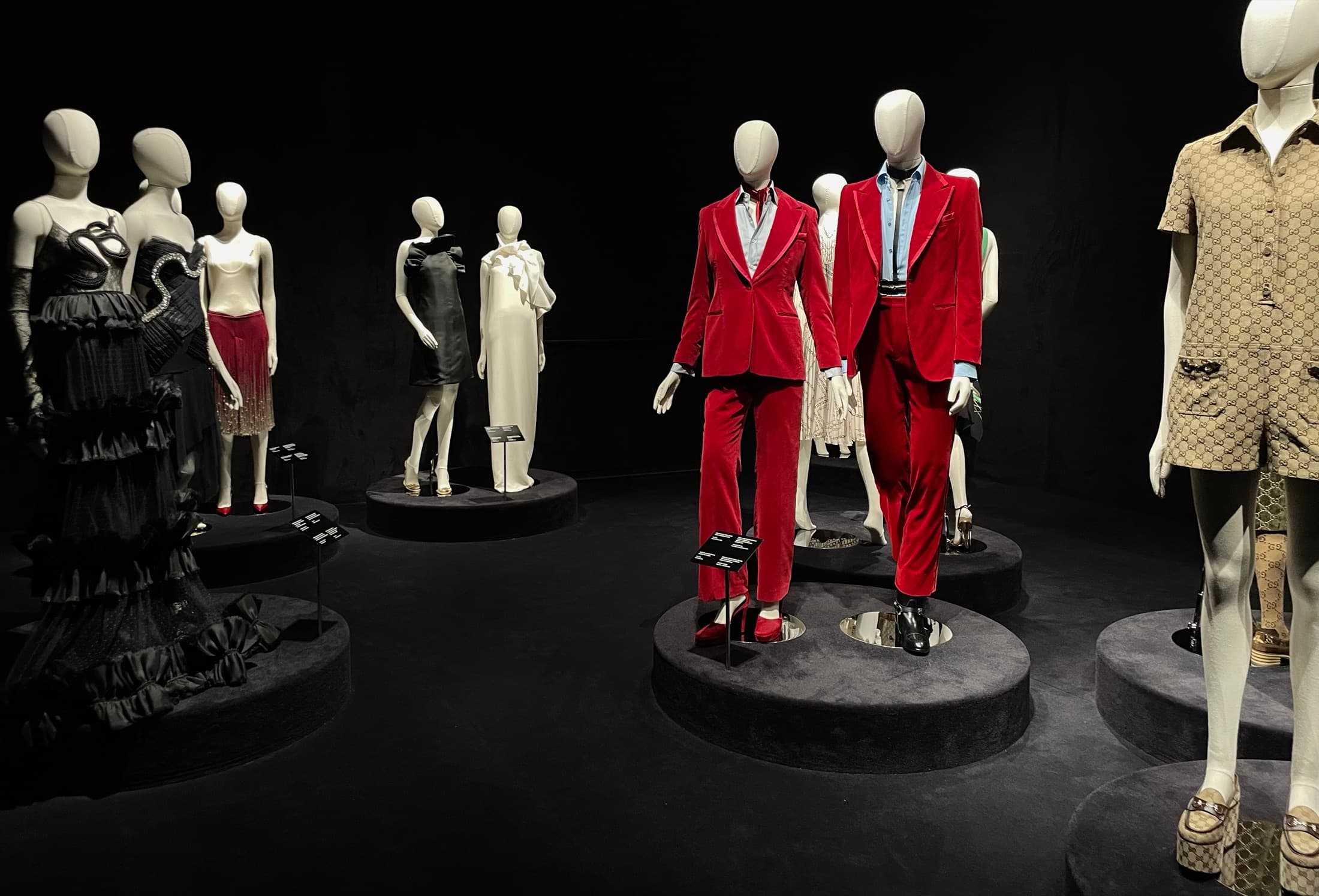Mannequins on low plinths in a dark room, two of them in red tailoring