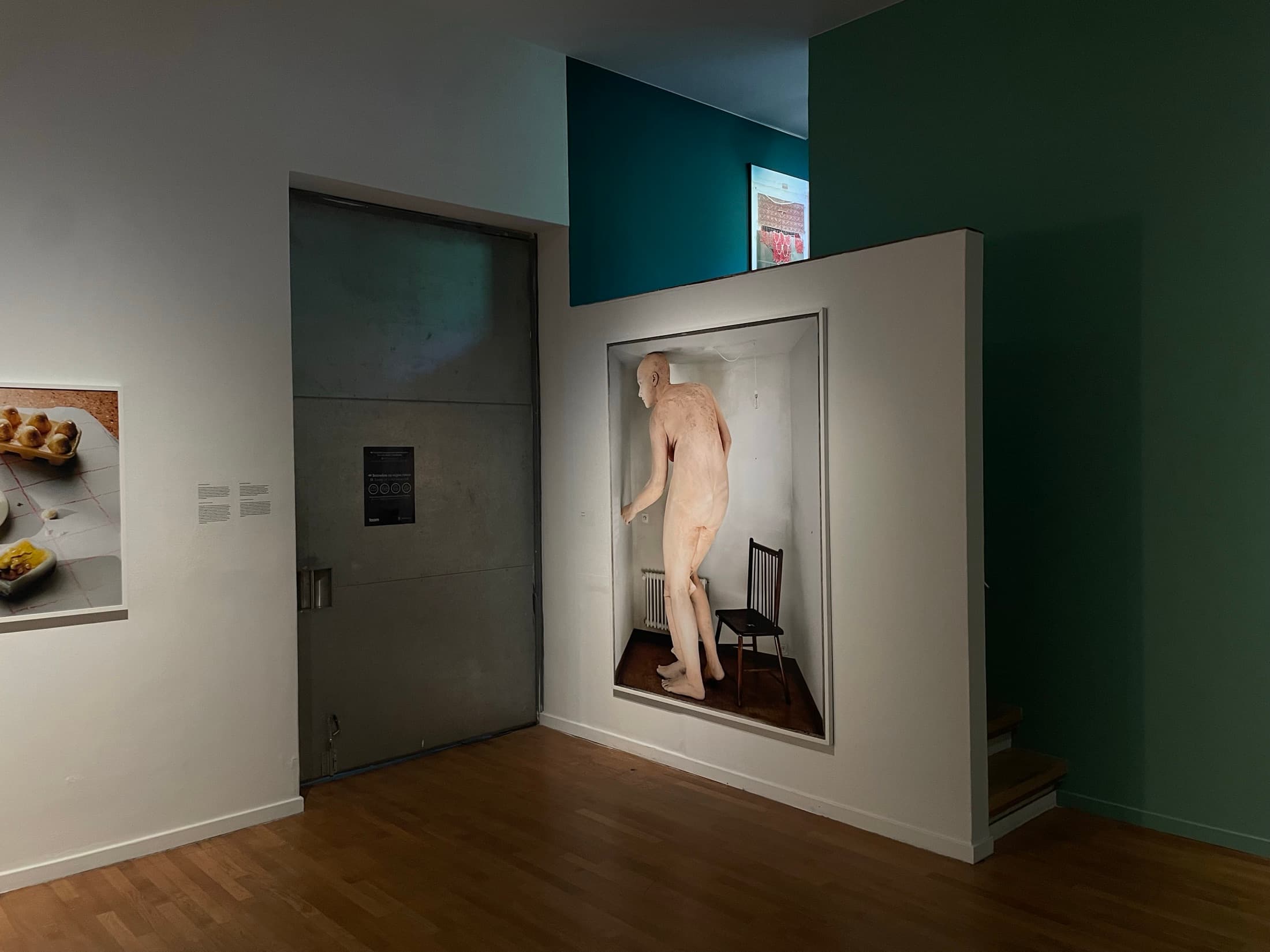 A museum room with a sculpted figure in a wall vitrine and teal painted walls