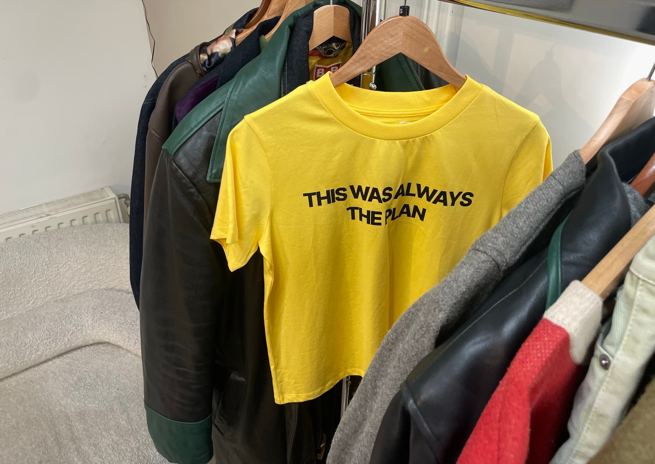 A rail of jackets around a yellow T-shirt printed 'This was always the plan'