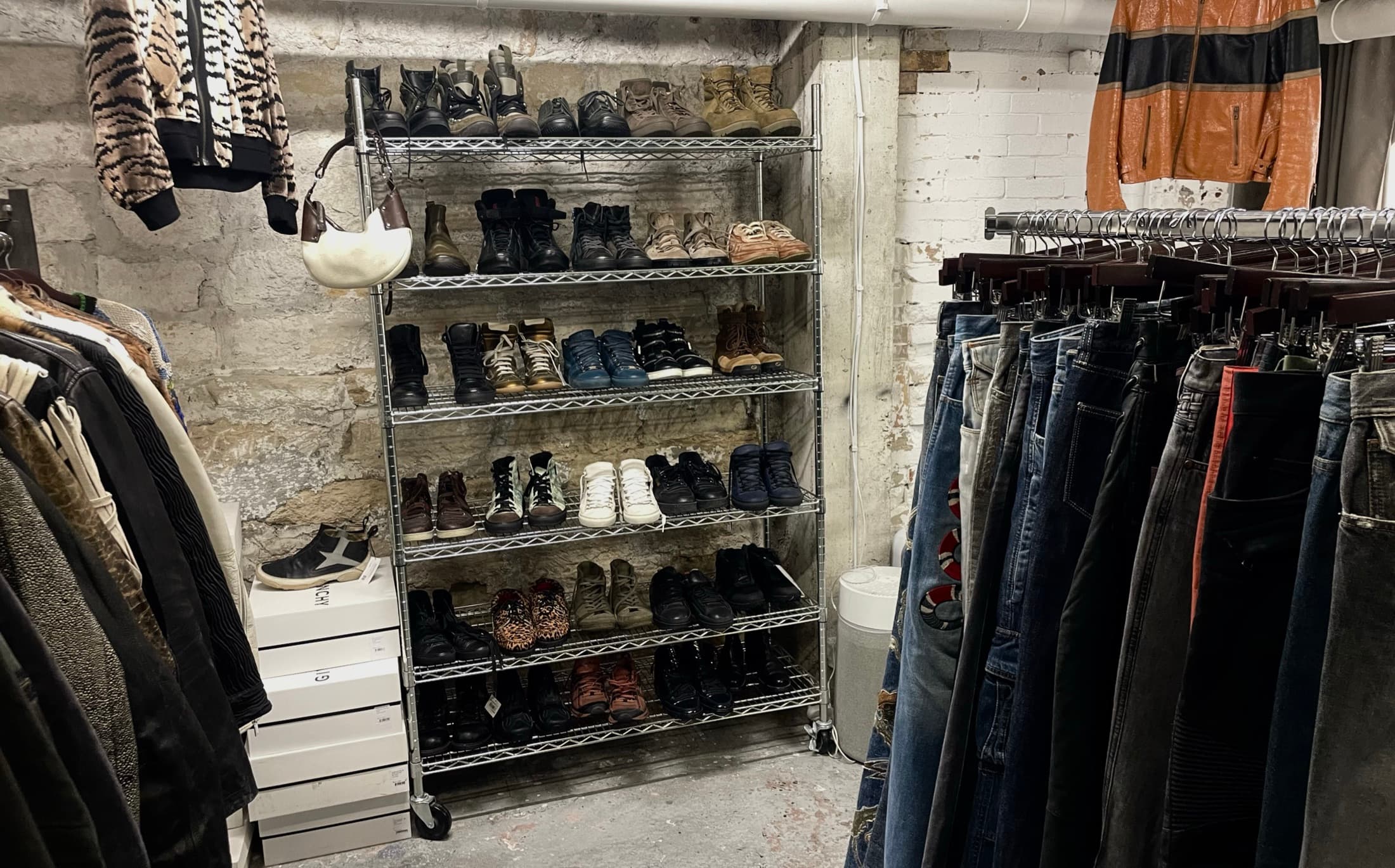A basement wardrobe room: rails of denim and leather against a bare stone wall