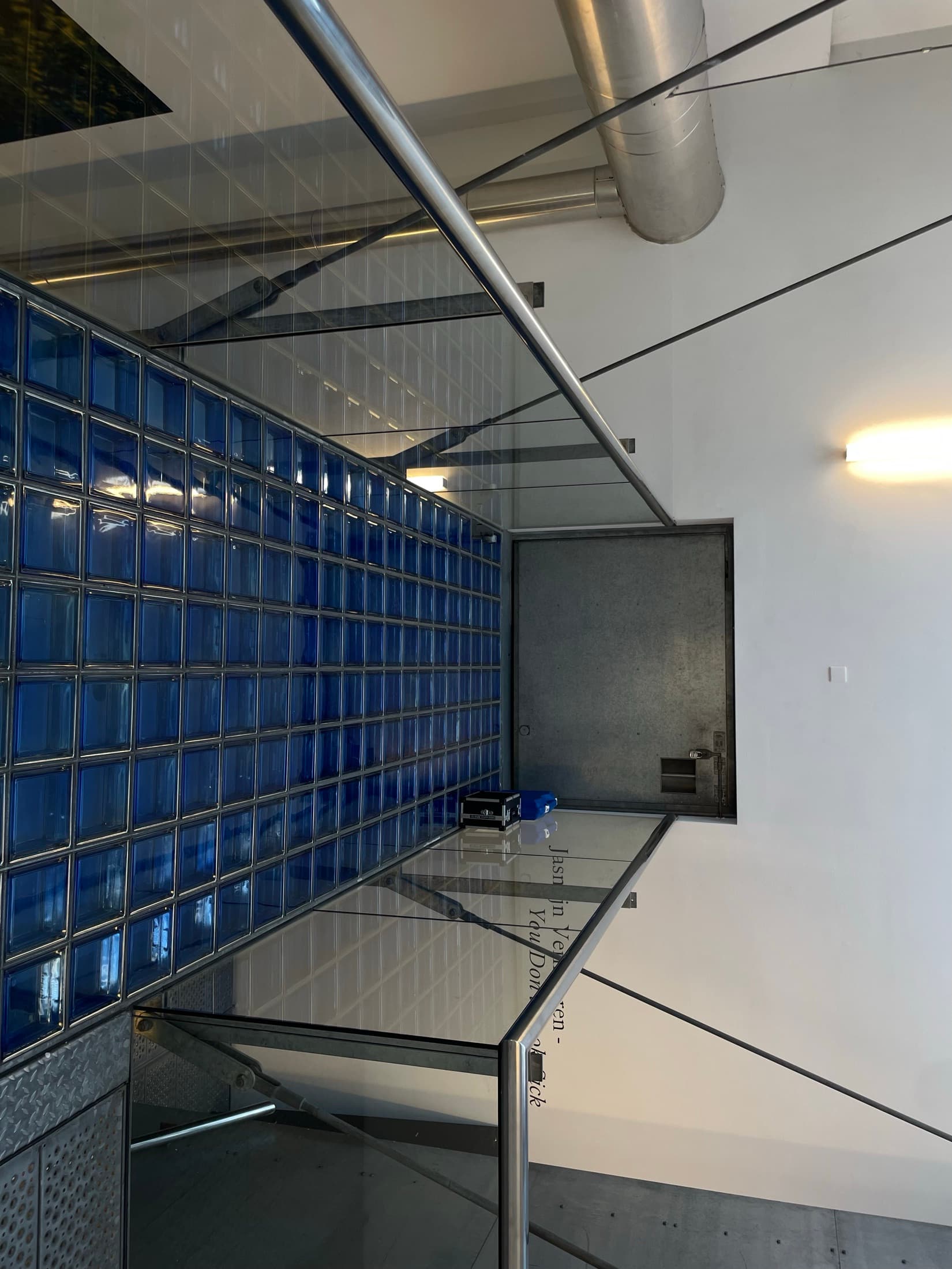 A wall of blue glass blocks beside a steel and glass stairwell