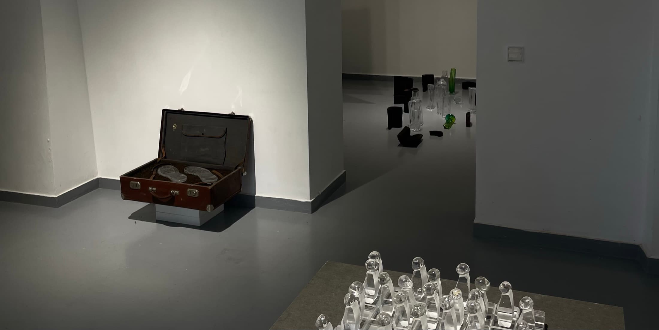 An open suitcase on the floor of a white room, glassware set out beside it