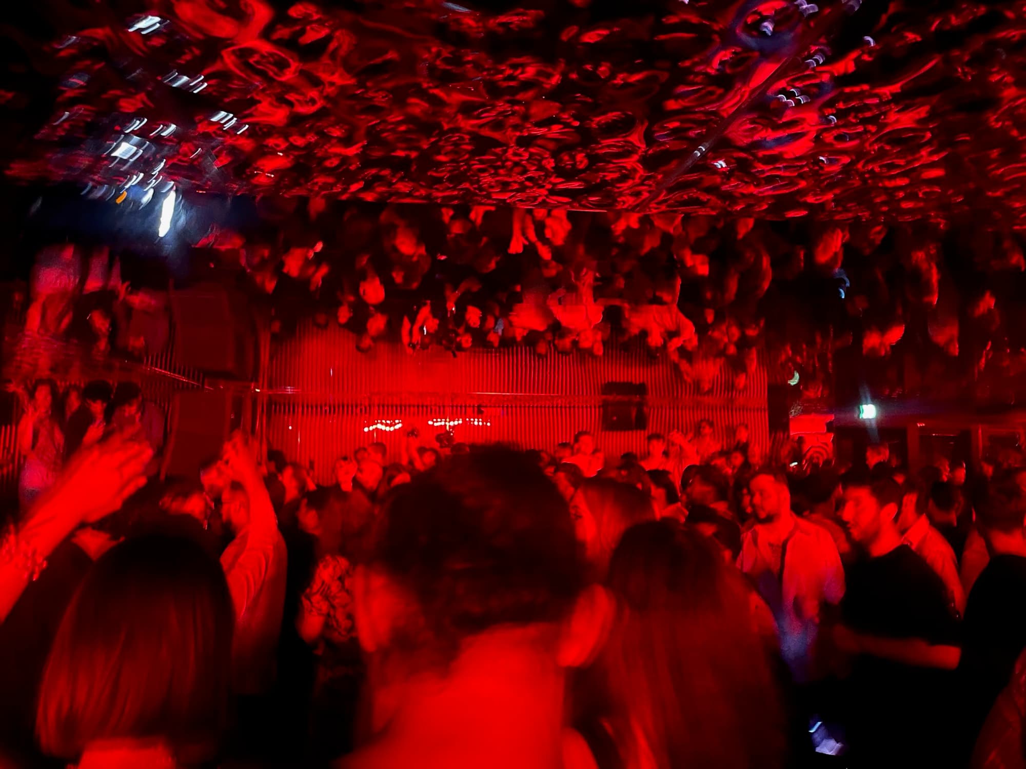 A packed room under red light, a mirrored ceiling above the crowd