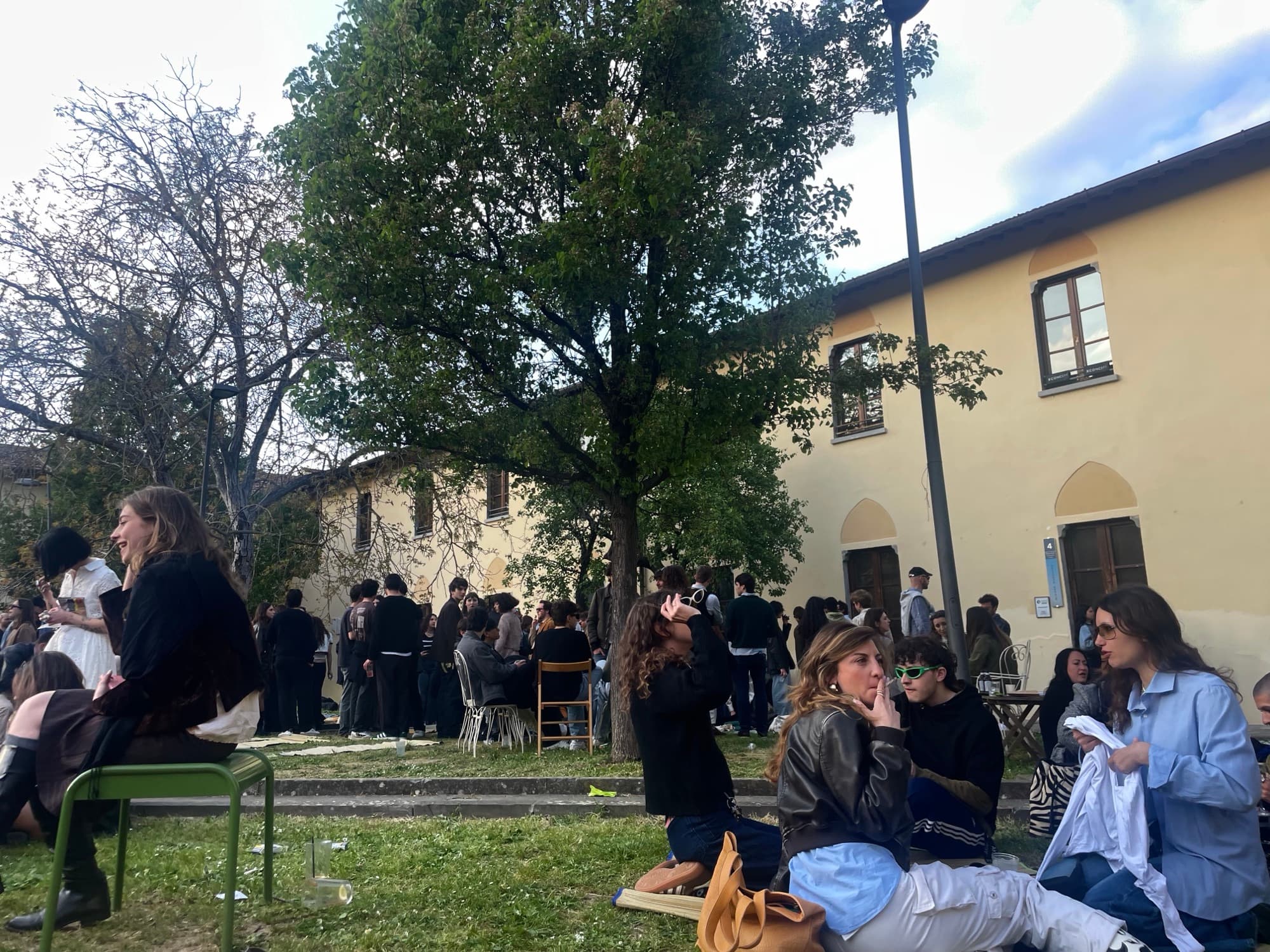 People sitting and standing on a lawn in front of an old villa