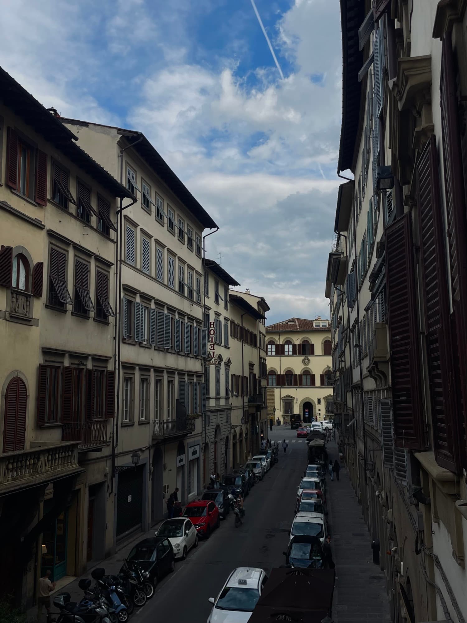 A narrow street of tall shuttered buildings under a clouded sky