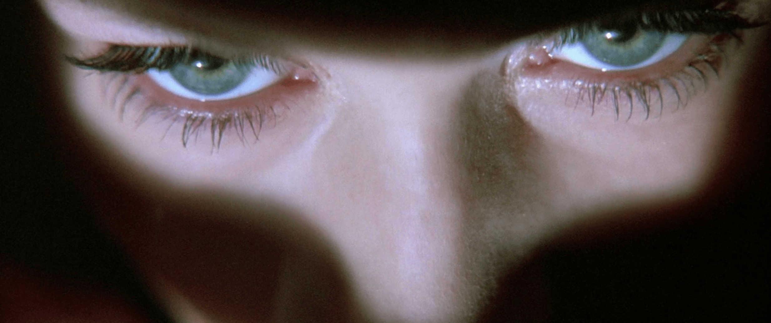 Extreme close-up of a woman's pale face and green eyes emerging from deep shadow, a still from the film Lost Highway.
