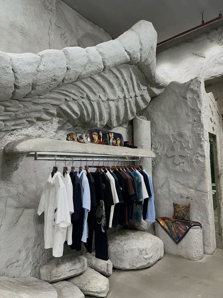 A retail interior carved to look like rock, a clothing rail slung beneath a stone ledge and garments hung against the pale wall.