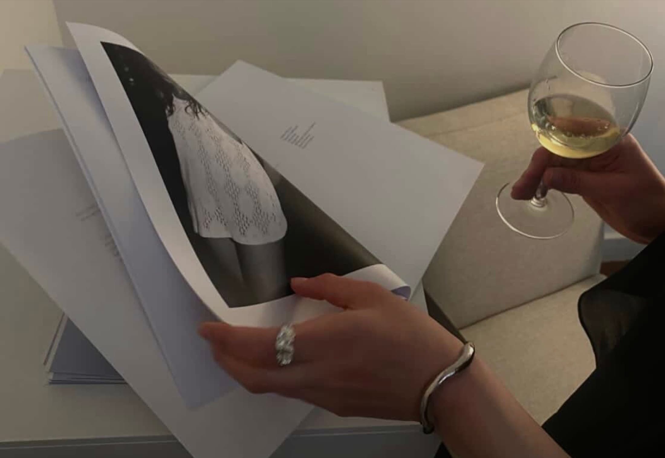 Hands turning the pages of a printed lookbook, a glass of white wine in the other hand