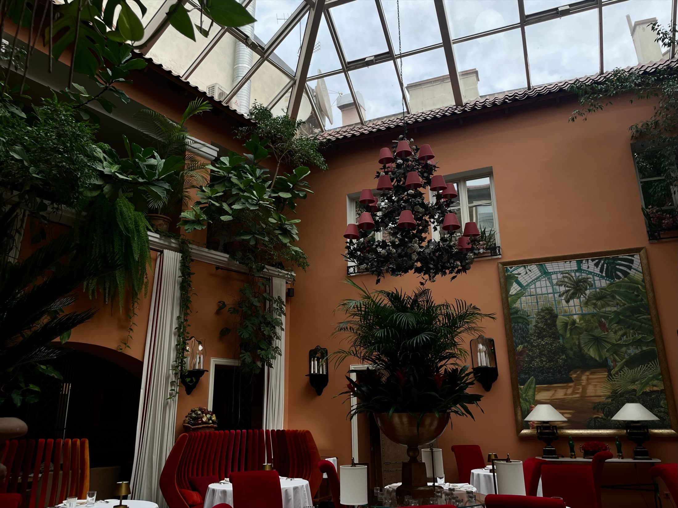 Laid tables and red banquettes under a planted glass roof