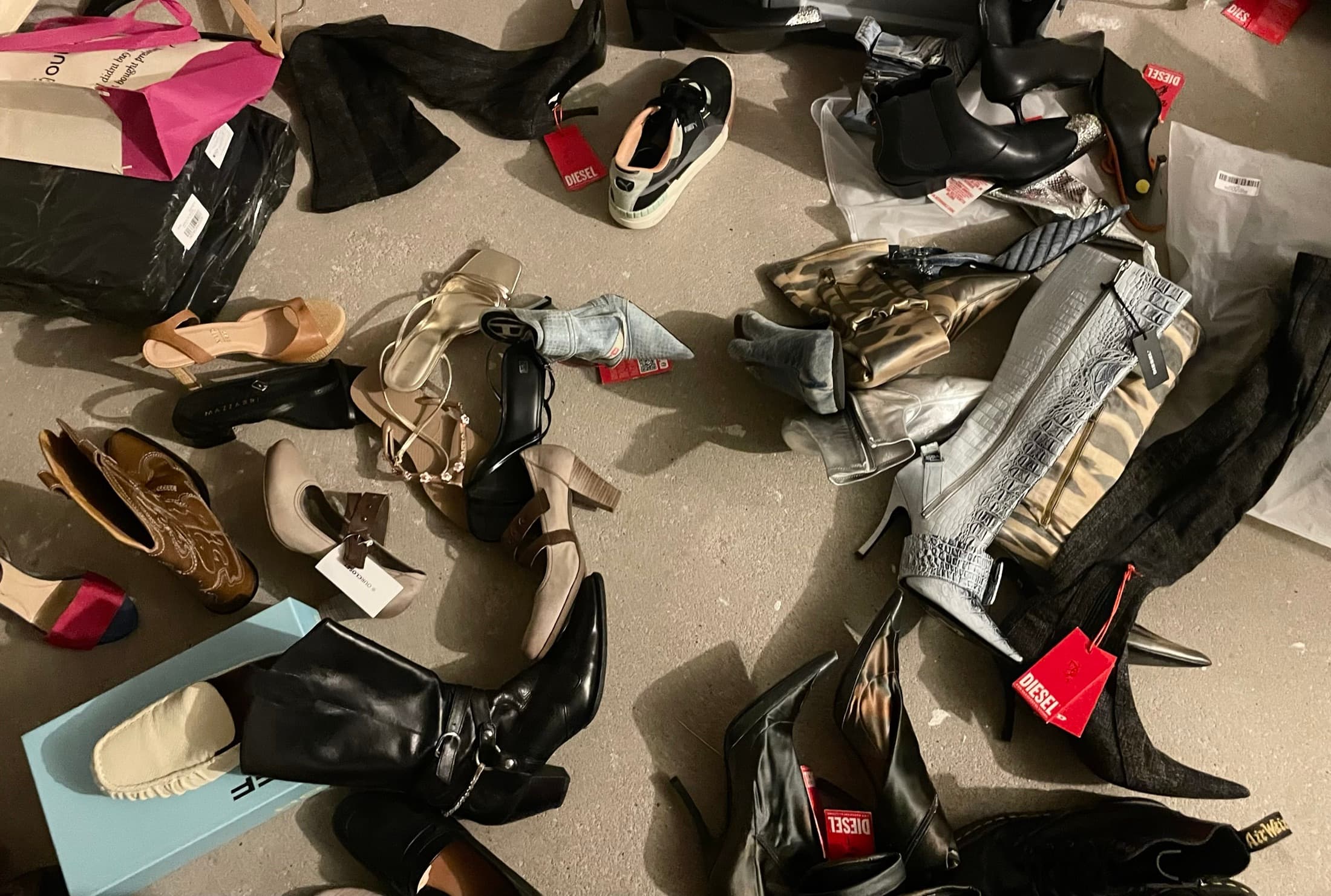 Shoes, boots and bags spread across a concrete floor, tags still on them