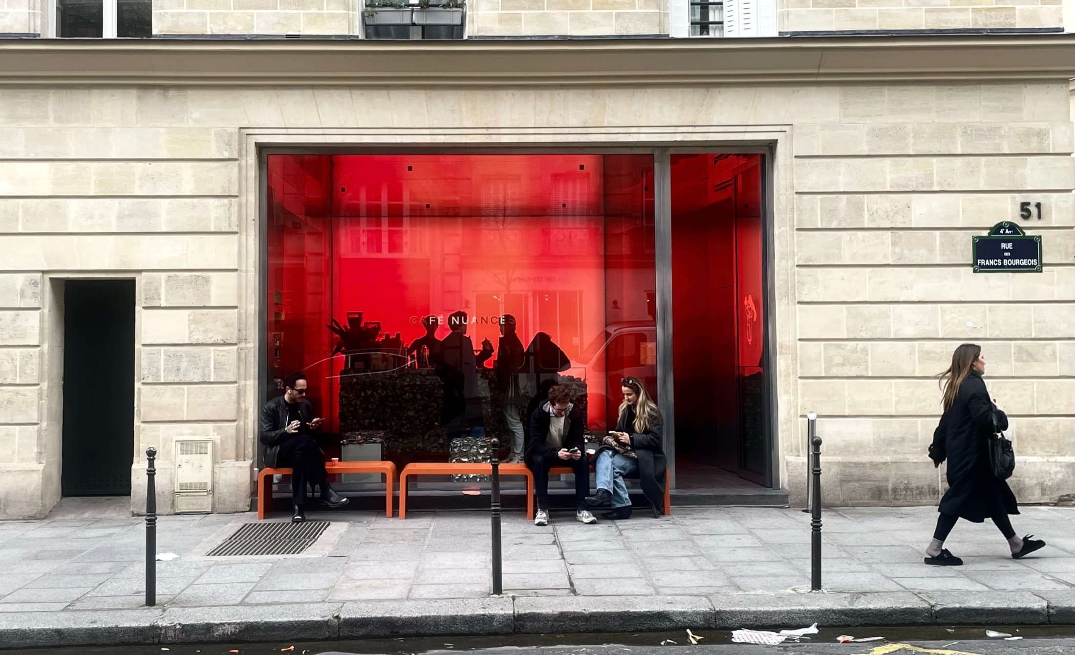 People sitting on benches outside a café behind a red glass front