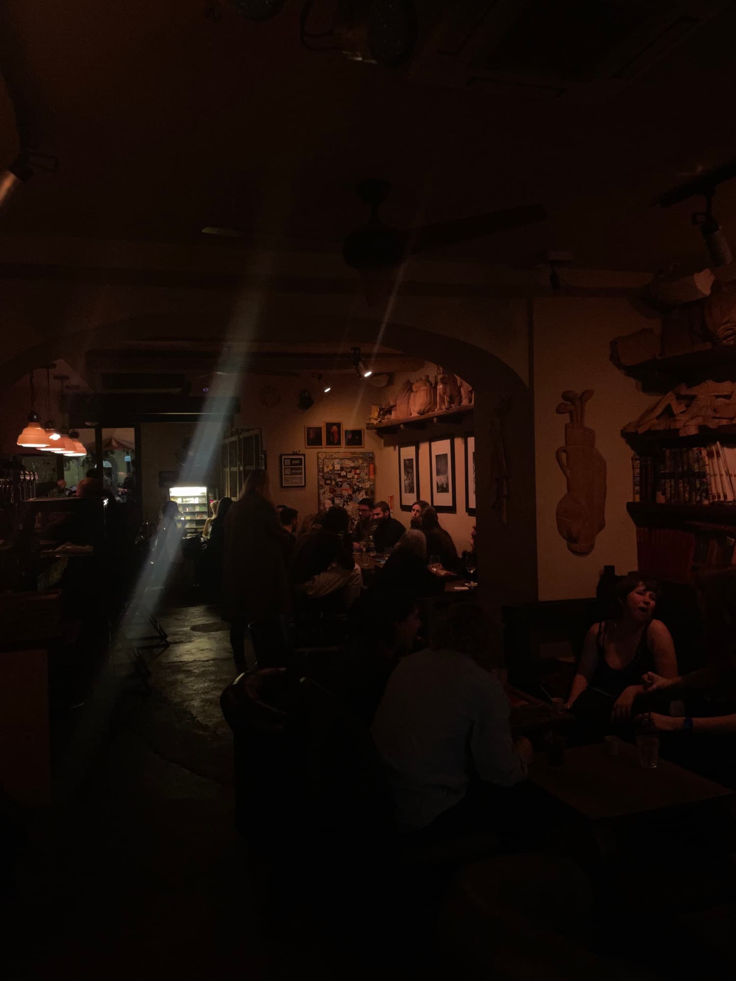 A dark bar, people at tables under one beam of warm light